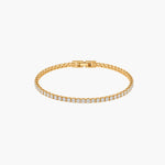 A gold tennis bracelet featuring a single row of round-cut clear gemstones, displayed on a clean white background.