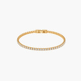 A gold tennis bracelet featuring a single row of round-cut clear gemstones, displayed on a clean white background.